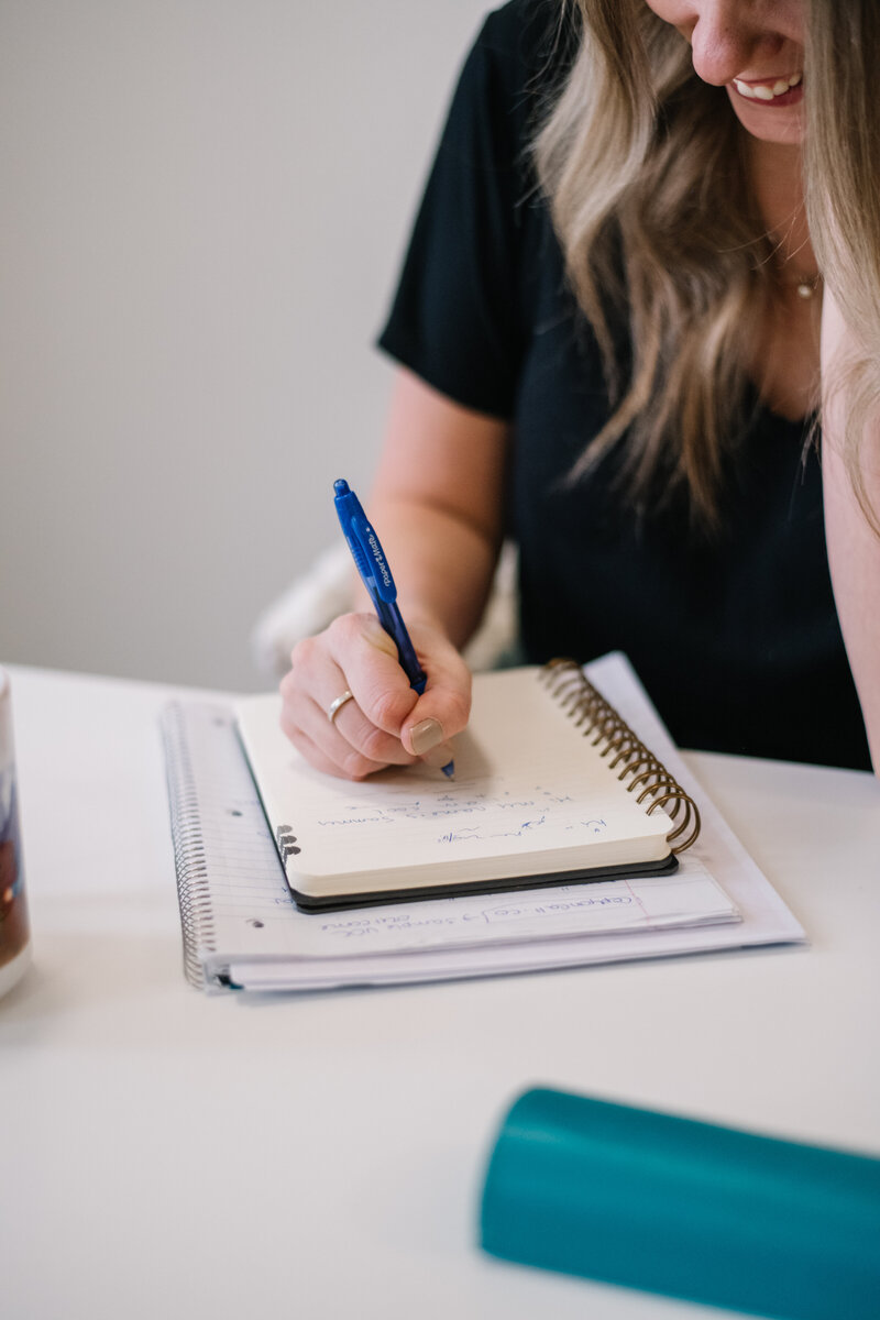 Hand writing on a stack of notebooks with a blue pen