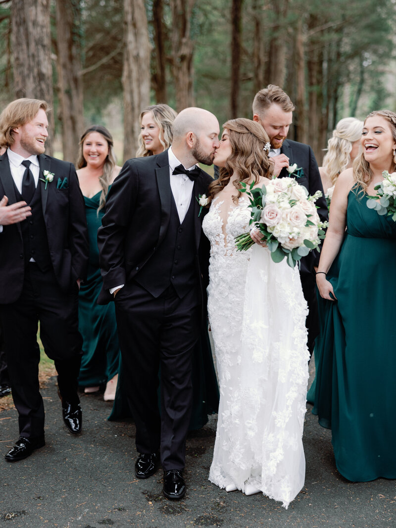A bride and groom share a kiss as they walk with their bridesmaids and groomsmen
