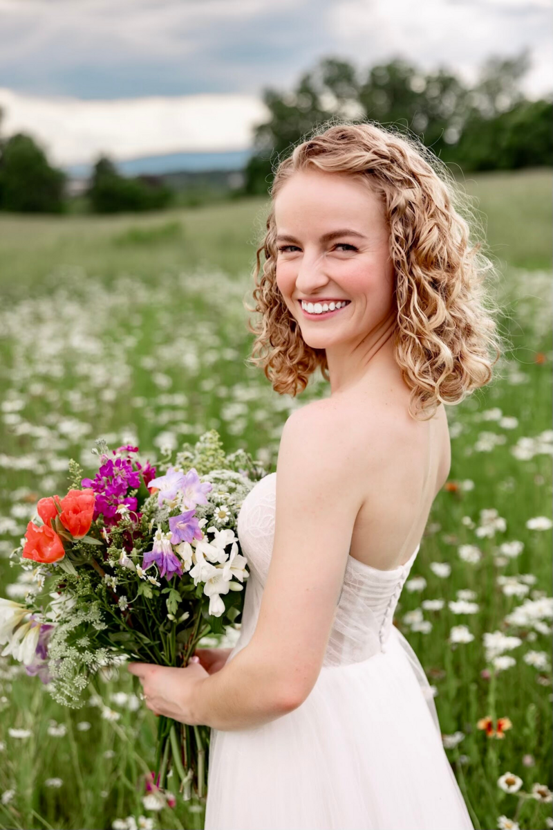 A bride stands in a field of wildflowers holding a bouquet