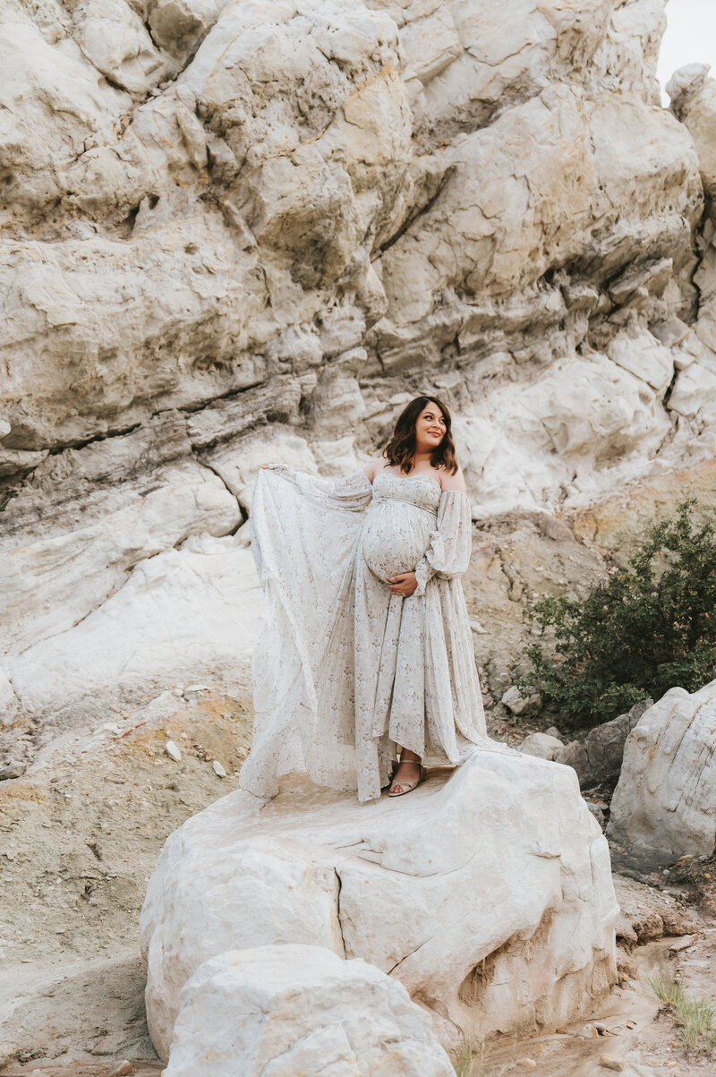 Woman on a rock holding her dress and baby bump