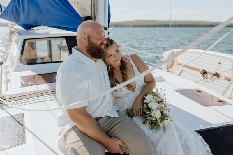 bride and groom sitting on a sailboat looking into the distance and smiling