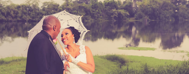 Bride holds vintage, white, lace umbrella as she smiles happily at groom in an outdoor shot. Photo by Ross Photography, Trinidad W.I..