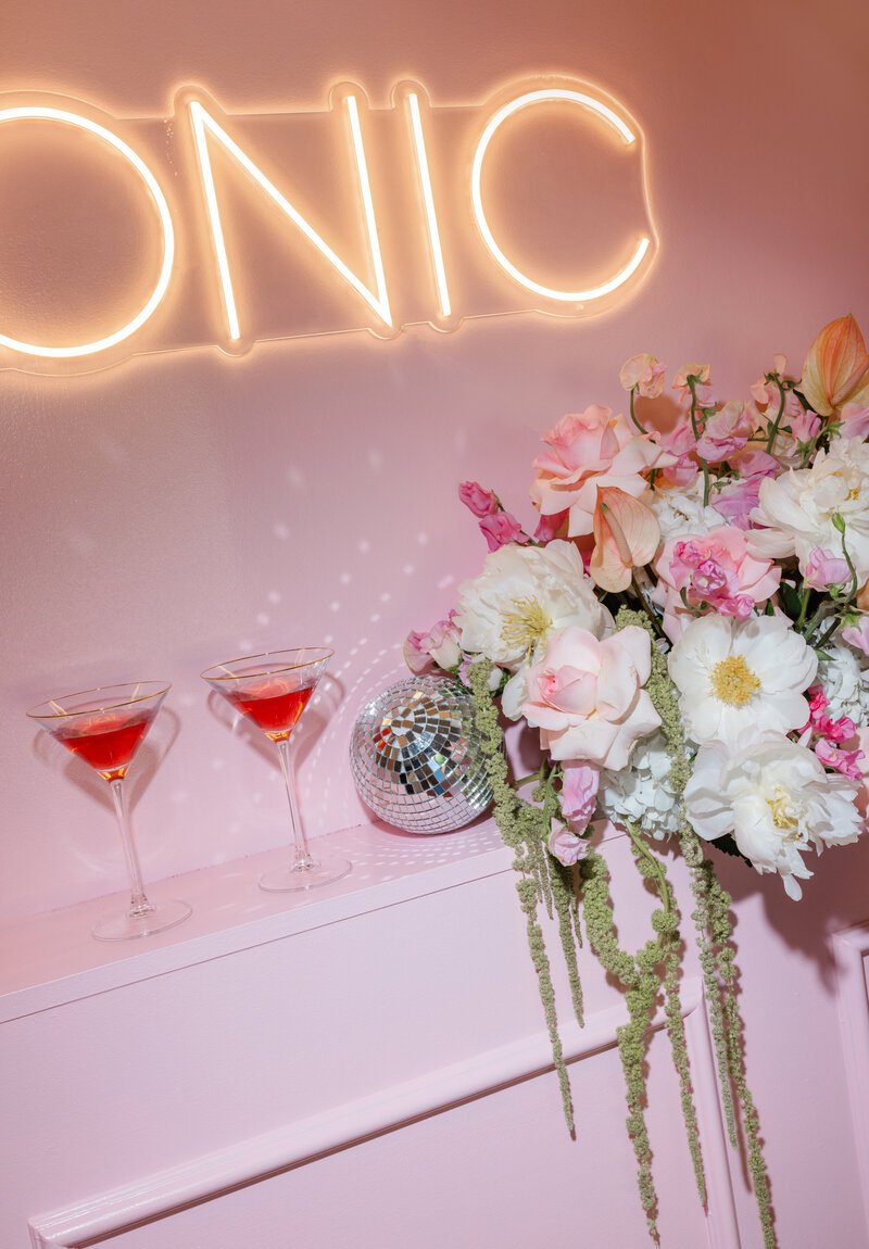 Close-up of a neon “ICONIC” sign, floral arrangement, disco ball, and two pink cocktails — glamorous retro detail captured by Greenville South Carolina portrait photographer Dani Lacey Photographs.