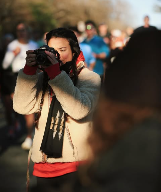 Photographer Courtney Claire Beglin capturing an event with a DSLR camera, surrounded by a crowd, representing her visionary photography process