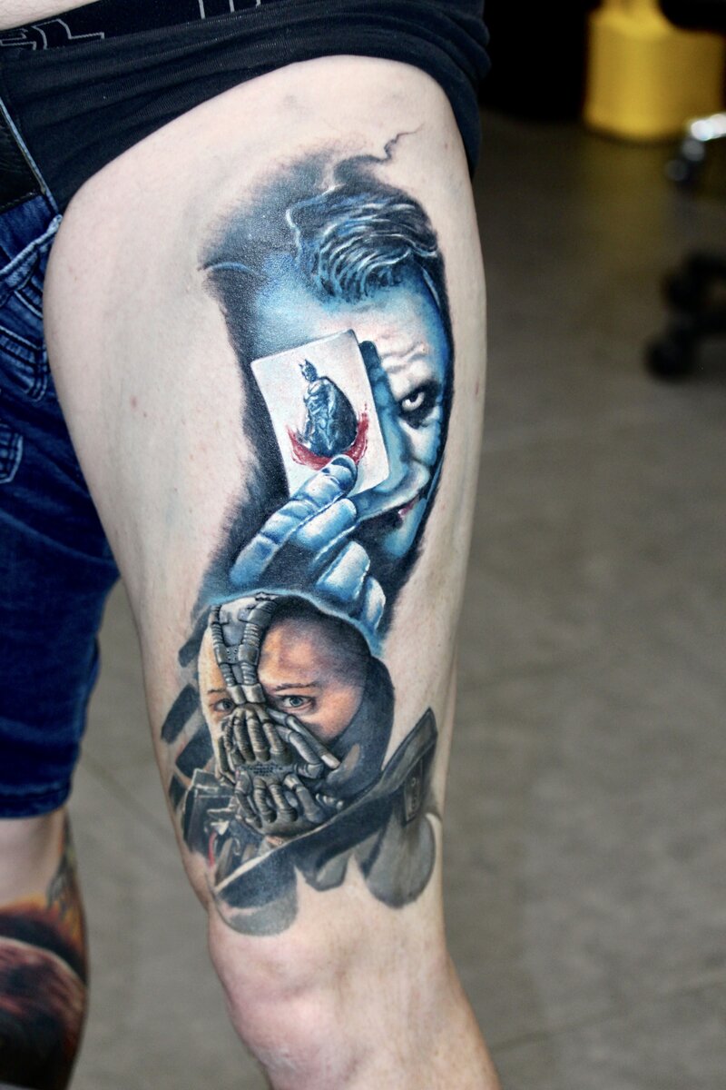 A striking tattoo featuring both Bane and the Joker, two iconic villains from The Dark Knight Trilogy. The design captures Bane's menacing mask and powerful presence alongside the Joker's chaotic grin and eerie expression, blending the contrasting personalities with intricate shading and bold lines to create a dramatic, dynamic composition.