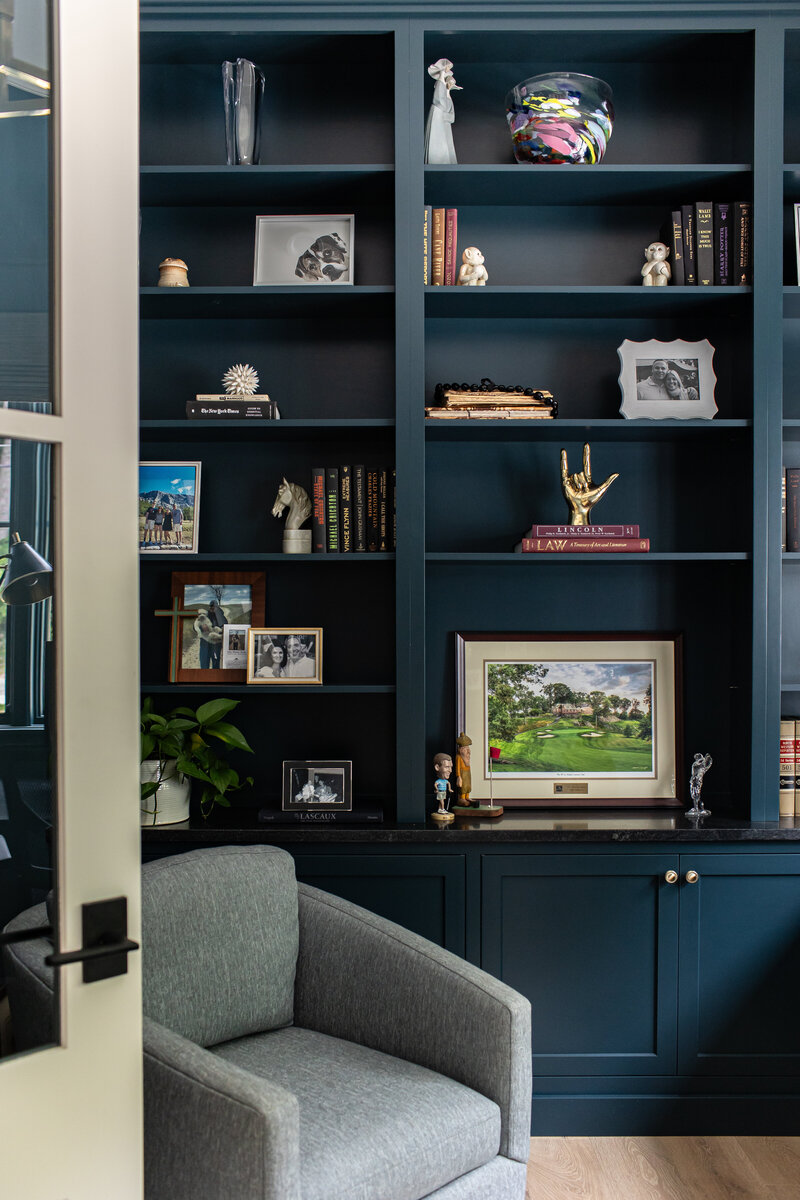 A sophisticated navy office featuring built-ins extending from wall to ceiling, with books and decor thoughtfully arranged on open shelving. The space is completed with a comfortable office chair, combining style and functionality for an inspiring work environment.