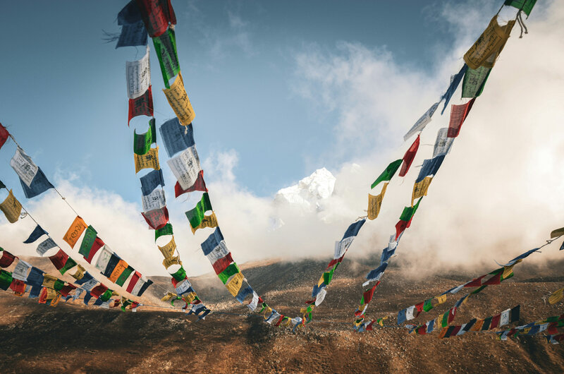 Colorful prayer flags fluttering in the Himalayas with snow-capped peaks in the background.