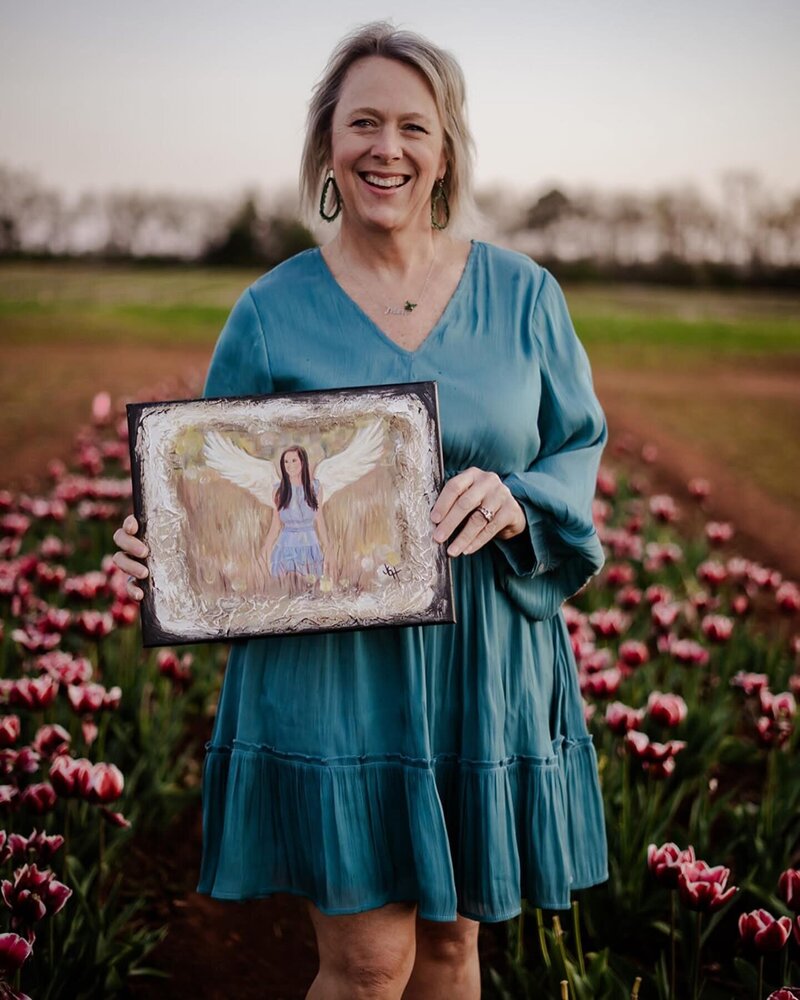 Blonde woman in blue dress holding painting in tulip field