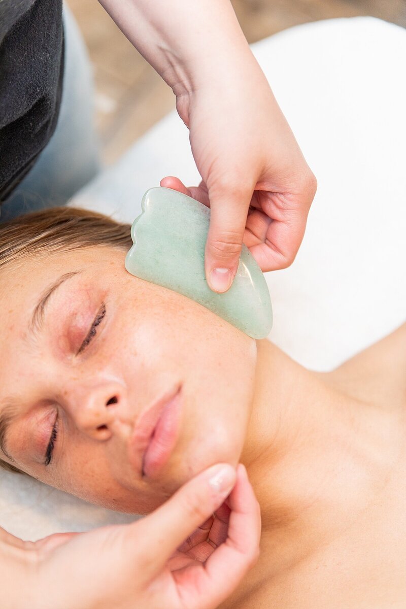 Esthetician, Rachel Smith, giving a relaxation facial with a mint gua sha on the client's face.
