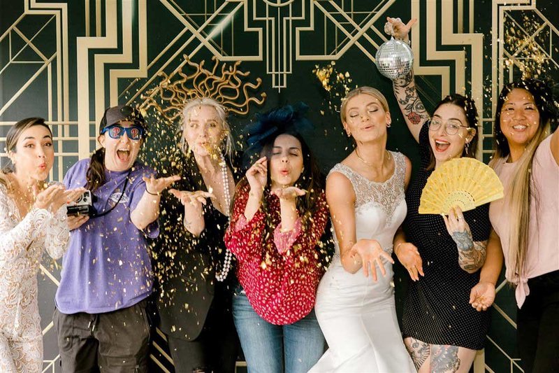 group of friends blowing confetti with a gatsby backdrop for a photo booth photo.