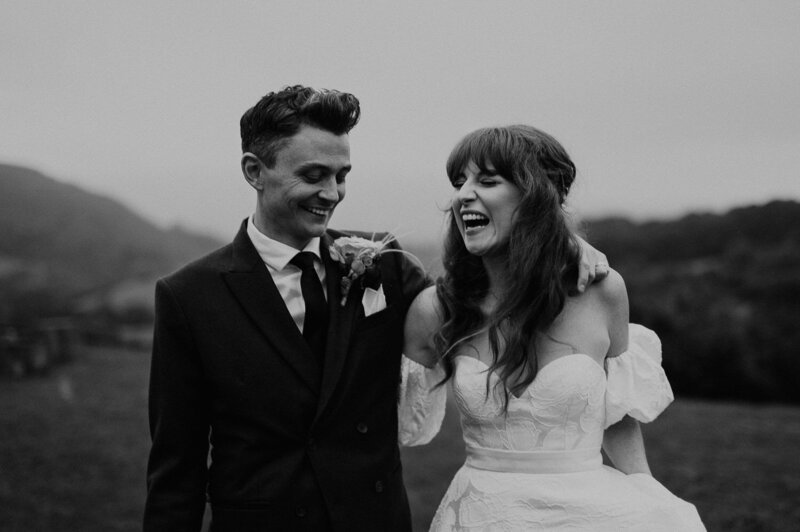 A bride and groom walk through the Welsh hills on their wedding day laughing.