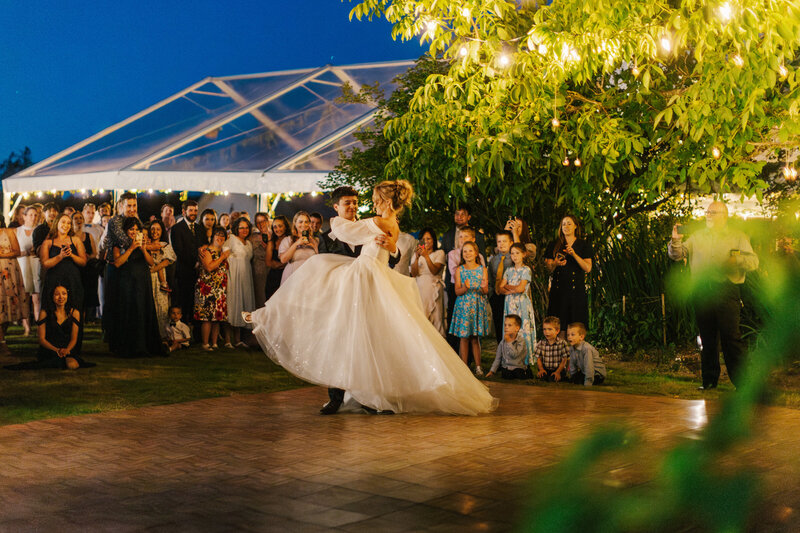 Groom spinning bride while dancing outside in front of wedding guests