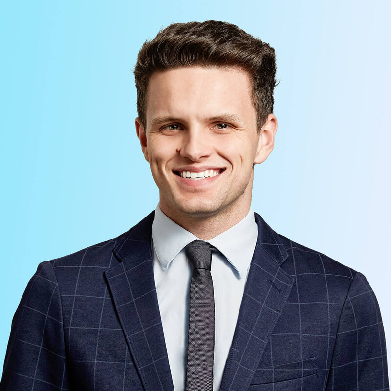 Studio shot of handsome man smiling wearing checked suit against a light blue and white gradient.
