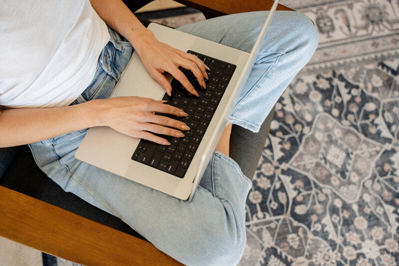 A woman wearing jeans sitting cross legged typing on a laptop