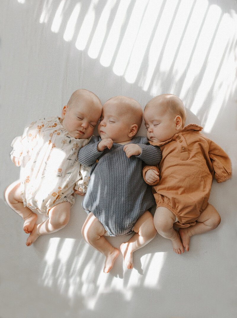 Three baby triplets sleeping on white sheet during St. Louis newborn photos