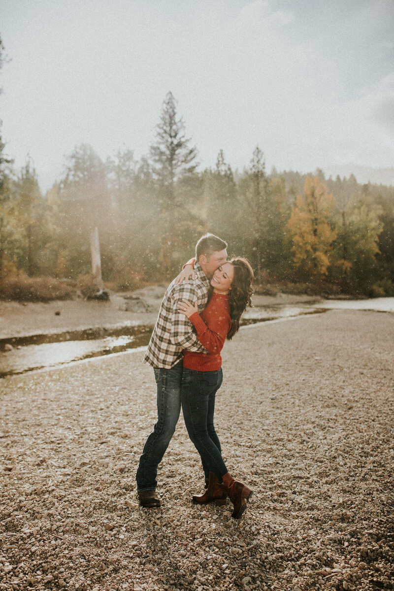 A man and woman wrap their arms around one another in front of a lake