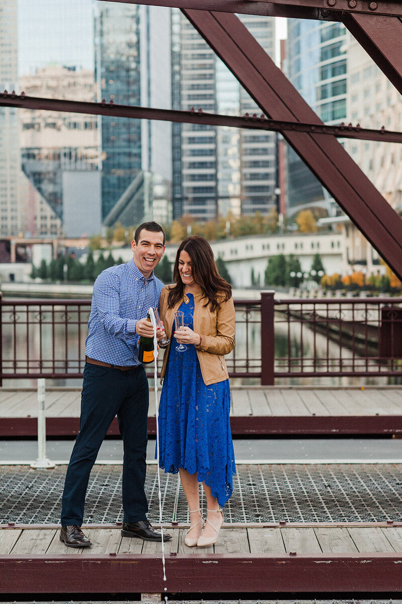 A couple pop open a bottle of champagne while standing on the Kinzie Street Bridge in Chicago