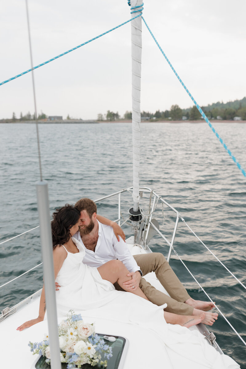 A couple sitting close together and about to kiss on the front of a sailboat 