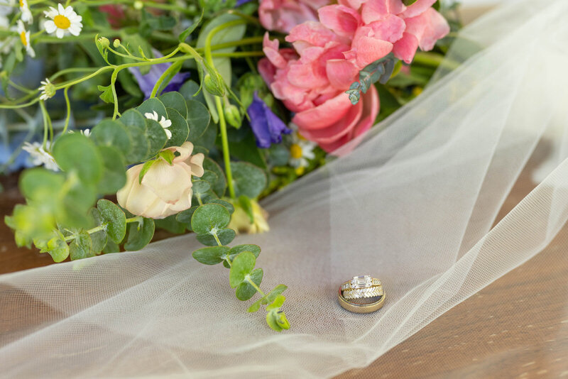 Wedding rings resting on veil next to bouquet