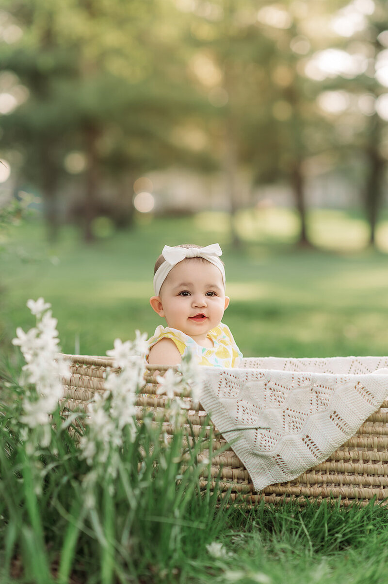 Baby girl wearing a lemon-print romper, sitting in a woven basket outdoors during a milestone session in Harrisburg, PA.