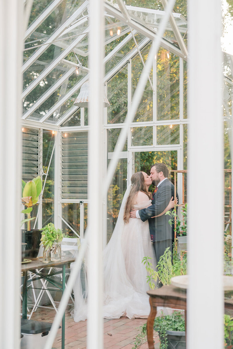 bride and groom kissing in a greenhouse