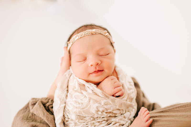 Springfield MO newborn photographer captures newborn baby girl smiling in her sleeping being held by mom