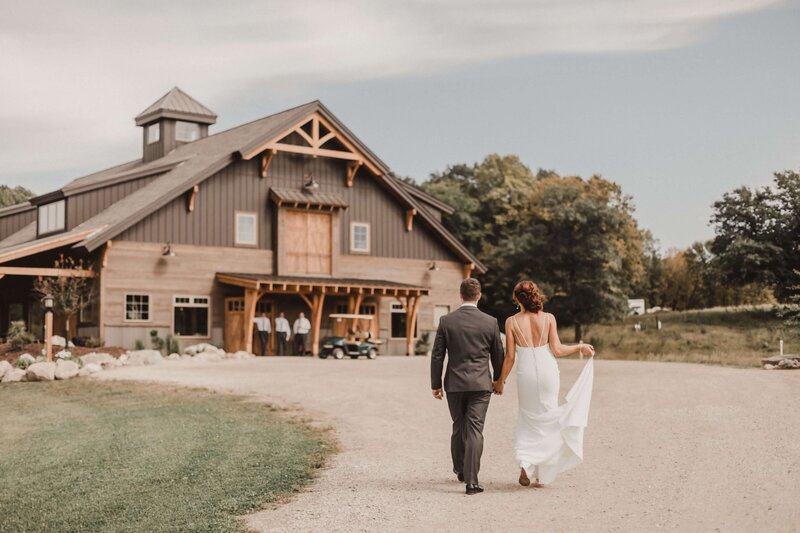 bride and groom walking toward barn wedding venue