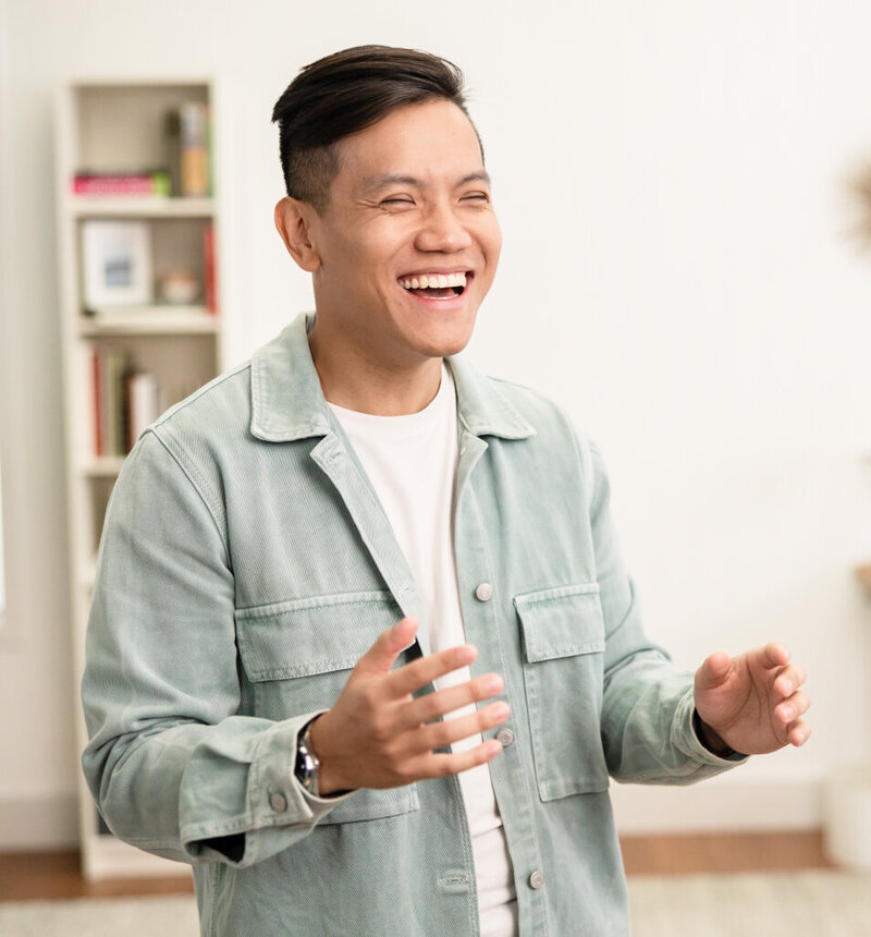 Sho Dewan, young Asian man, career coach and founder of Workhap, wearing a white tshirt and a light green thin jacket, laughing with his eyes closed