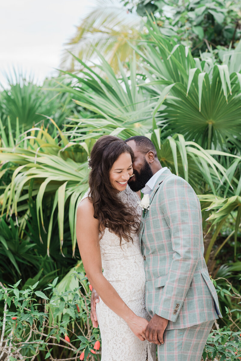 groom holding his brides hand as he whispers into her ear and she laughs photographed by denver wedding photographer as they stand in a tropical garden in denver botanic garden wedding