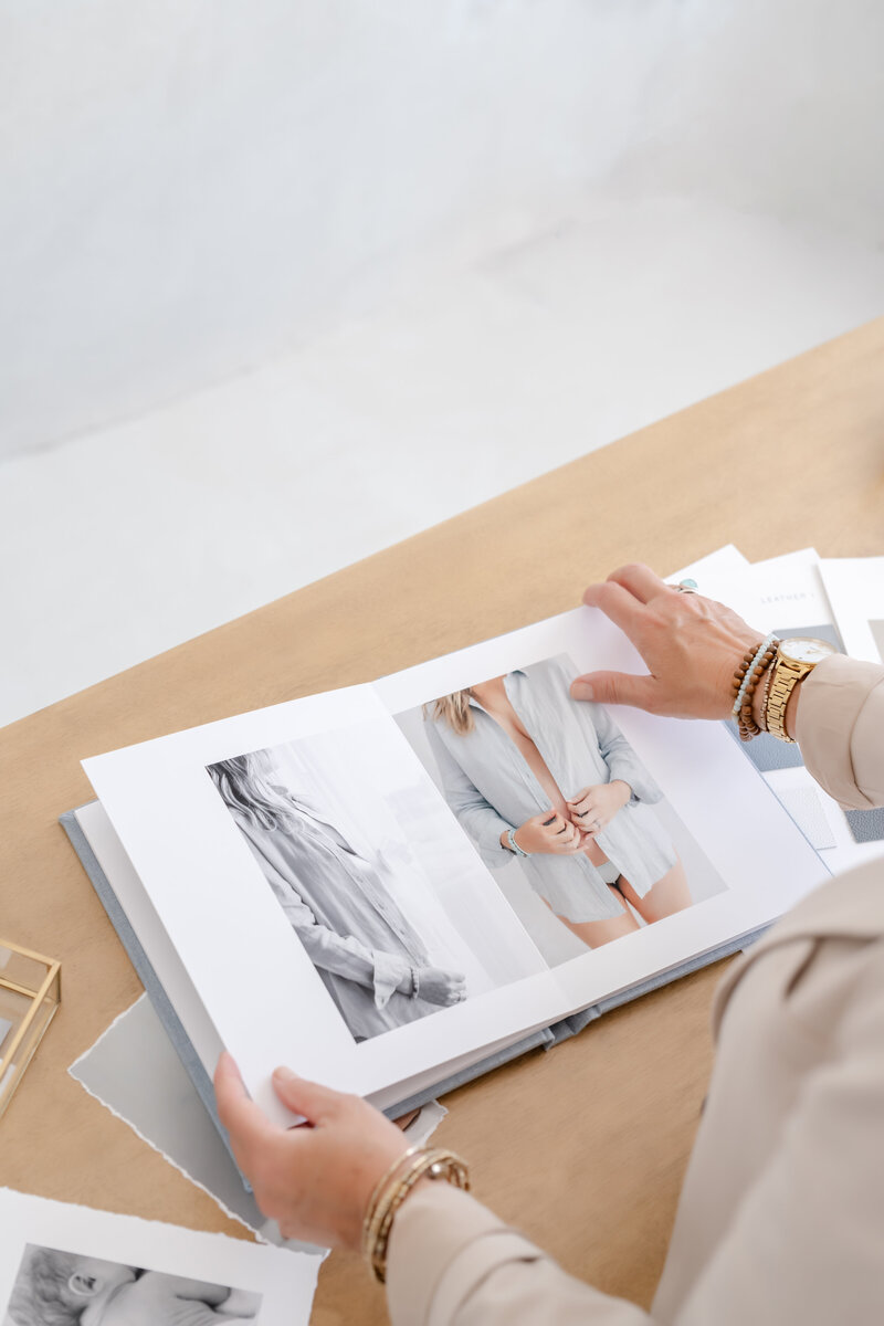 A woman flips through a luxury photo album featuring elegant maternity portraits during a design appointment with Little Palm Photography Studio in Northern California.