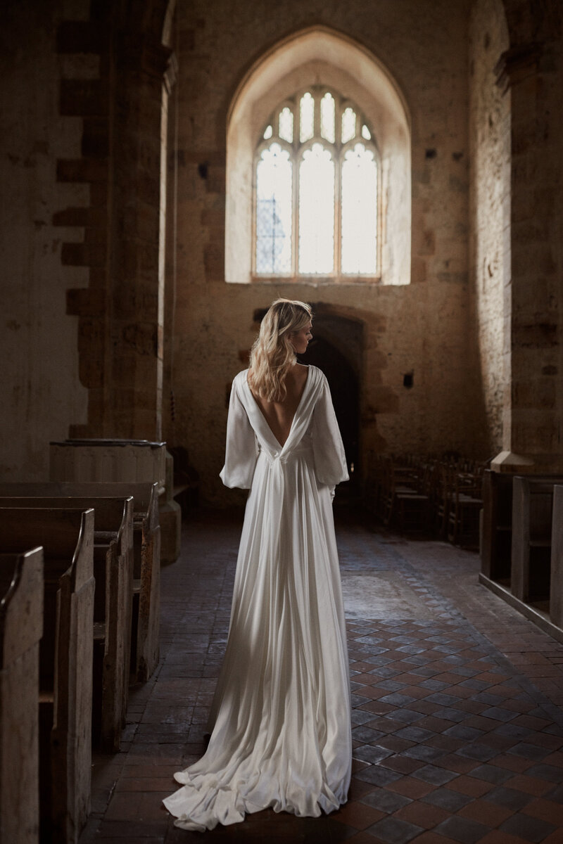 Long-sleeved silk wedding dress with deep v back worn by bride at wedding in church