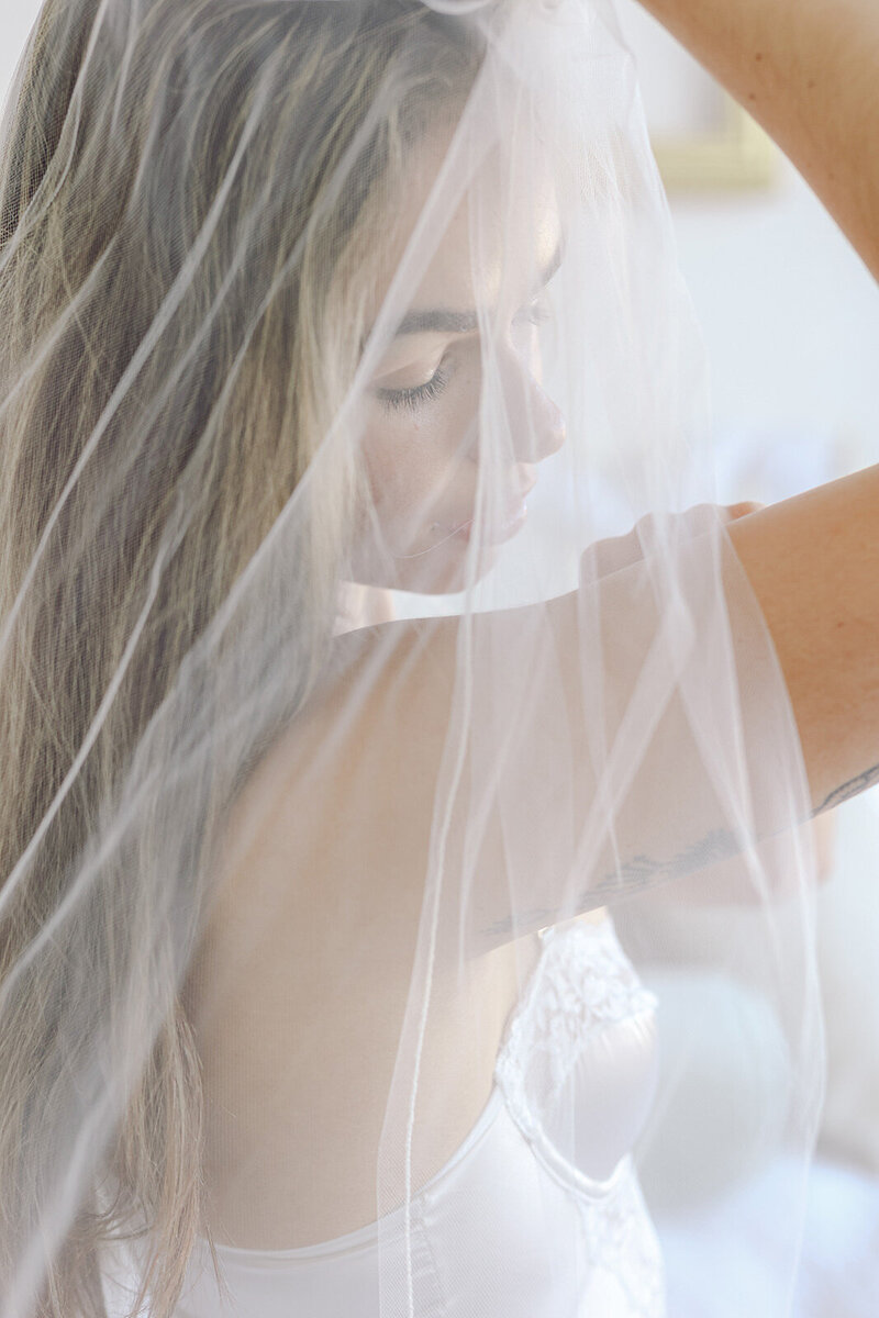 Girl posing in white lingerie elegantly photographed in a boudoir session. She is wearing also a bridal veil