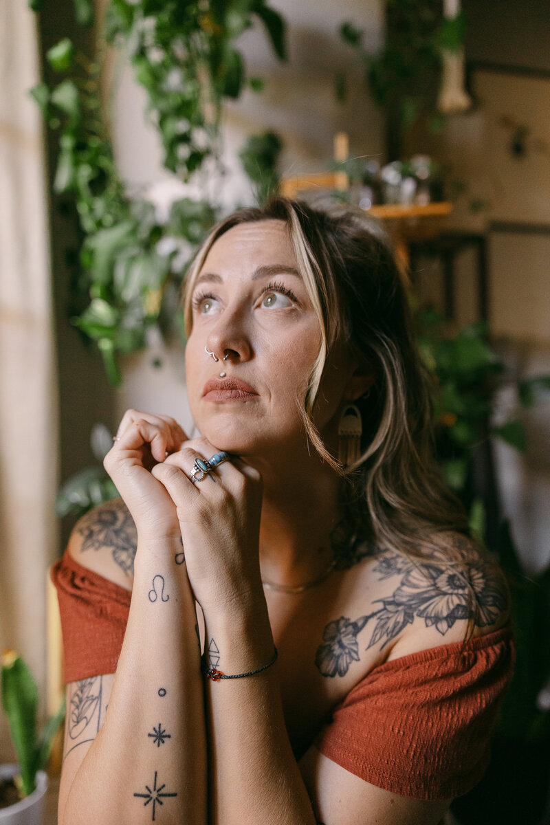 A woman with her hands under her chin as she looks up to the side.