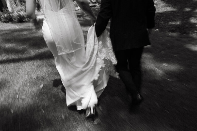 Artistic black-and-white image of a bride and groom walking hand-in-hand, capturing the intimate and timeless essence of their wedding day