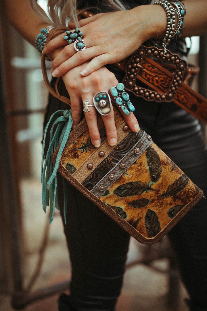 Hand with turquoise jewelry holds a leather clutch