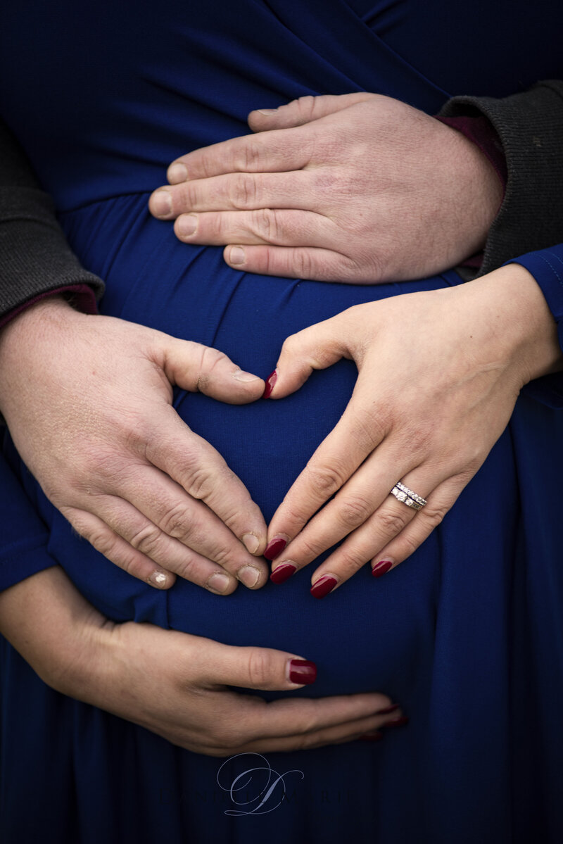 Maternity session in a park. Husband and wife make a heart over baby bump.