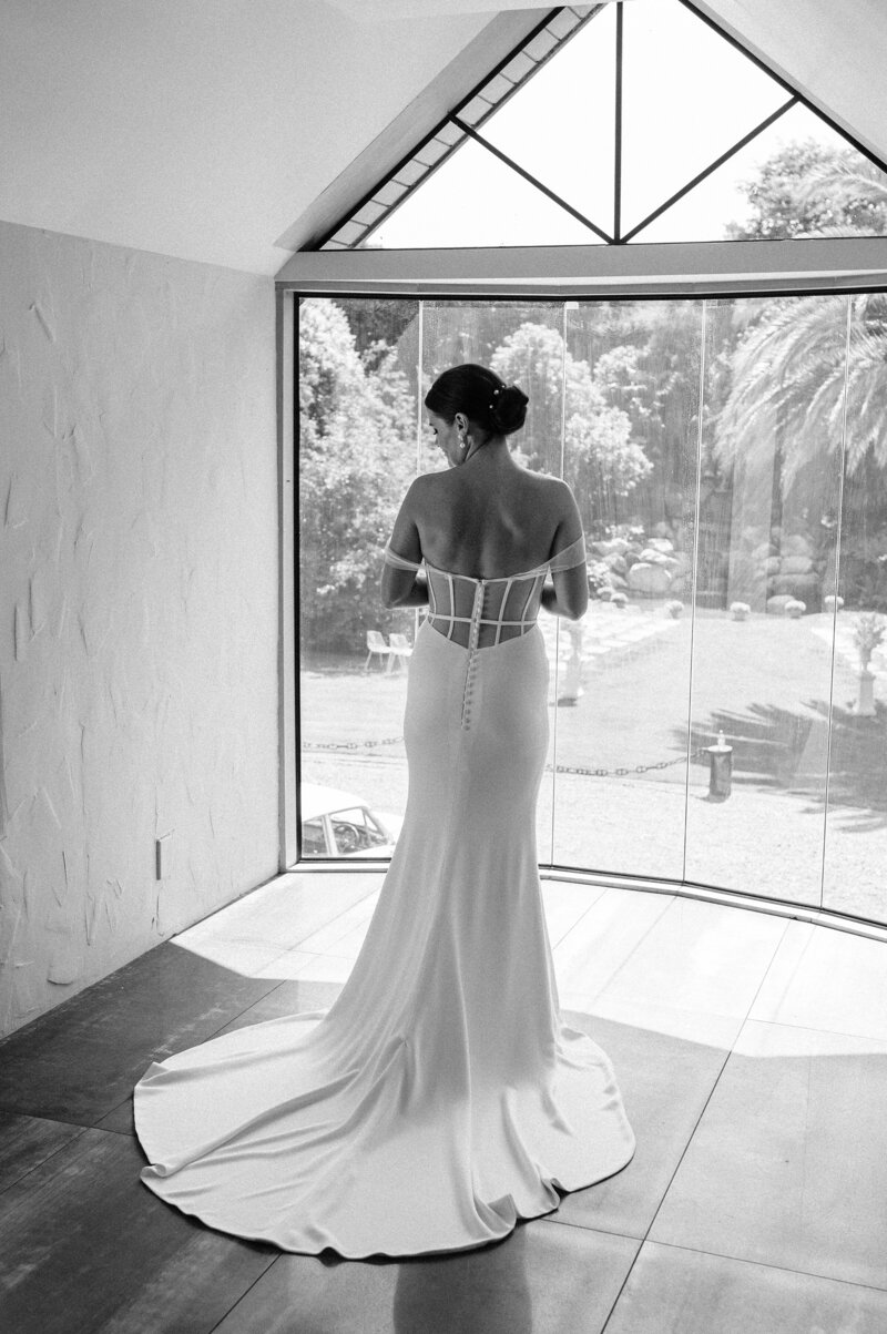 black and white photo of bride in trish peng dress looks over backyard ceremony setup in christchurch