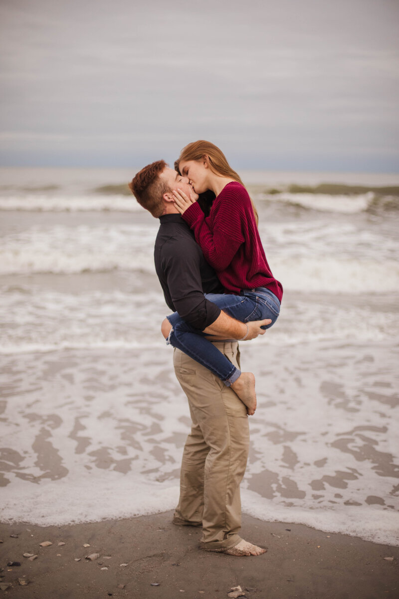 man and woman kissing on the beach during engagement session