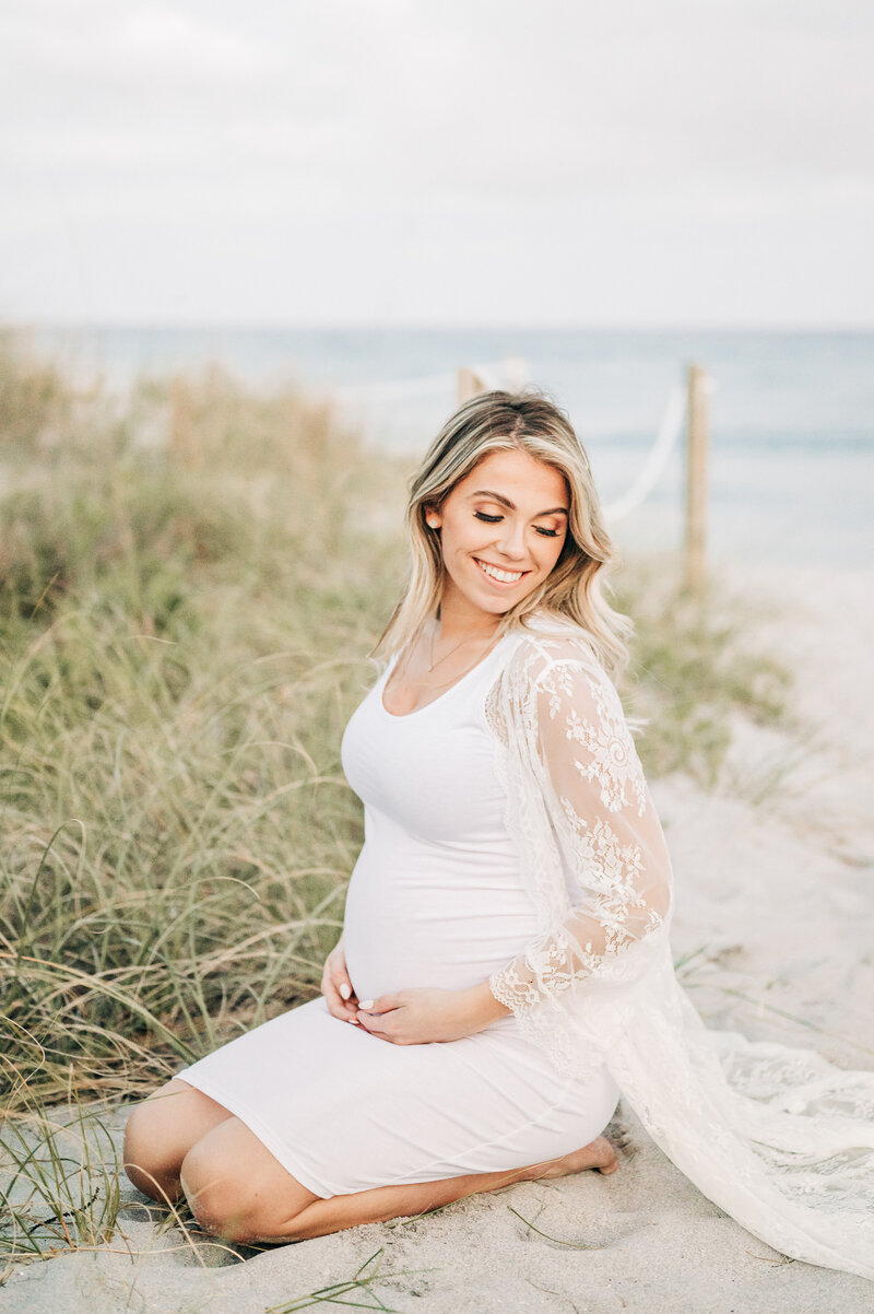 South Florida Maternity Photographer captures mom to be holding belly sitting on the sand