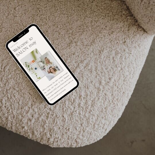 phone on a white boucle chair with a website for a hair salon