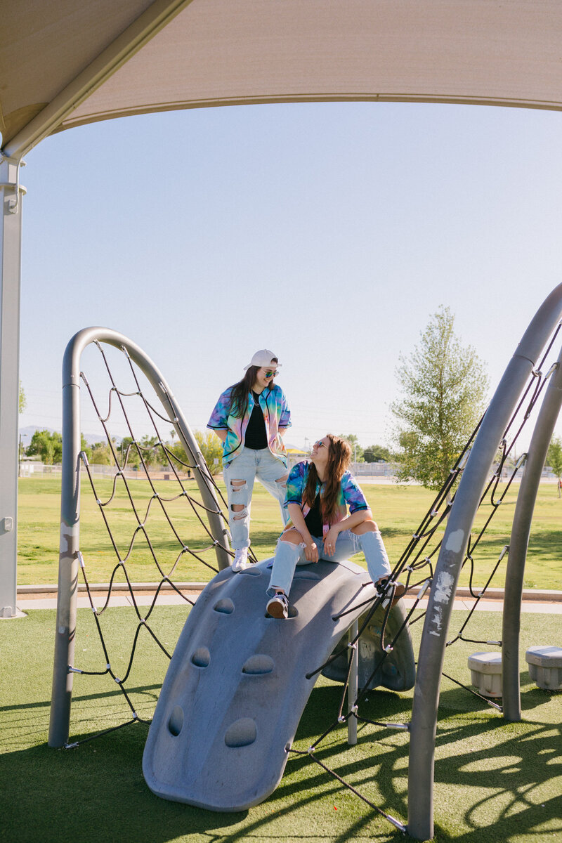Two people sitting and standing on playground equipment.