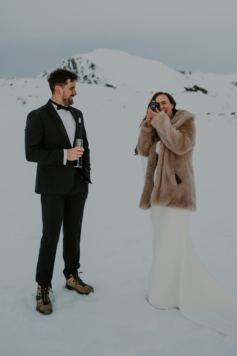 newlywed couple pose with camera on mountaintop