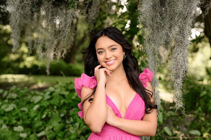 the bright pink dress on this charlotte senior stands out against the spanish moss drapped from the trees during her portrait session