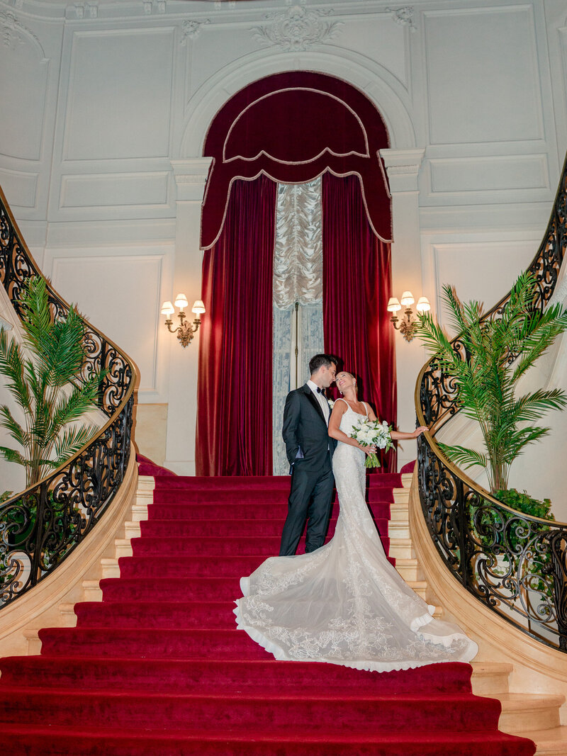Bride and groom on the red stairs in Rosecliff Mansion's entryway