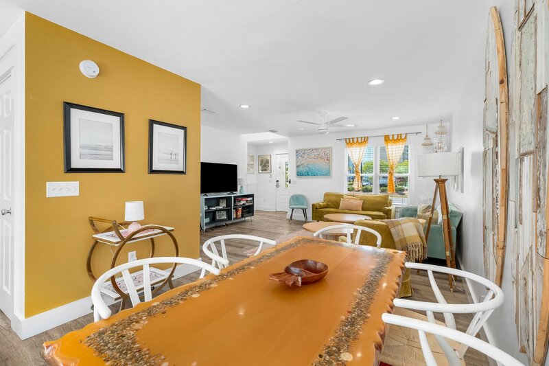 Open-concept view from dining room toward living room at the Pink Door Surf House, showcasing vibrant decor and mustard accent wall.