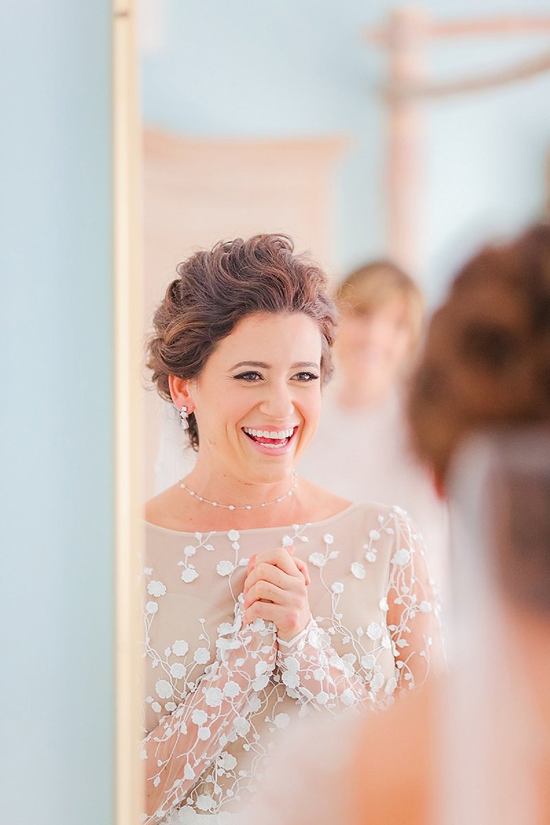 bridal portrait with excited nearly newlywed clasping her hands and smiling at her appearance in the mirror