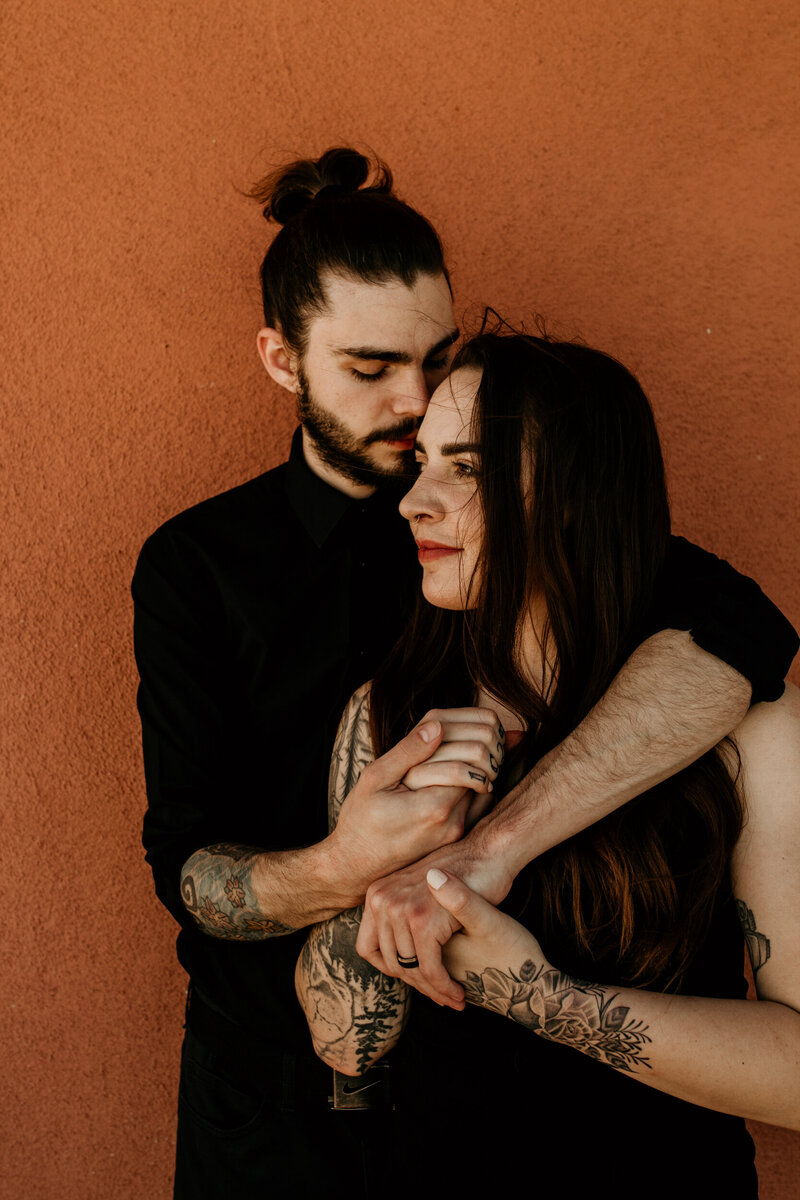 tattooed couple holding each other in front of an adobe home