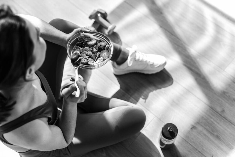 Woman sitting on the floor eating a healthy bowl of berries and cereal after a workout, emphasizing nutrition and recovery.