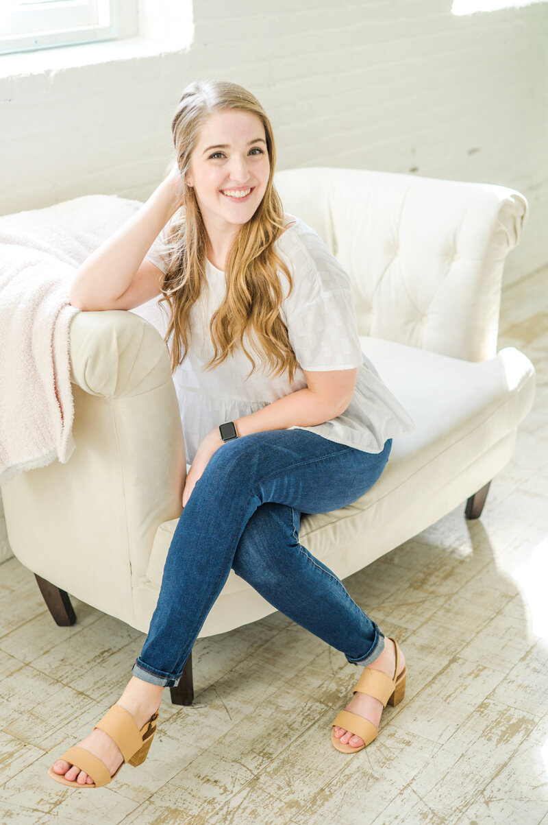 Cait Kramer is a Baltimore Wedding Photographer and smiles on a cream couch;