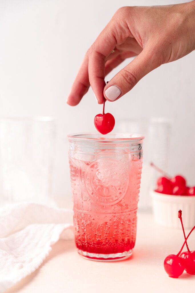a Shirley temple in a glass being topped with a cherry